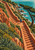 Terracotta stone stairs zigzag down a green coastal slope, with a tiny traveler in a blue coat and turquoise sea beyond.