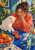 Young woman in a coral robe leaning toward a white cat reaching for a blood orange on a cobalt-blue table.