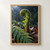 A rain-beaded unfurling fern crozier rises above fallen leaves, with a mature frond crossing the foreground.; frame shown for styling only