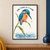 Turquoise and coral kingfisher perched on a curling green reed, watching a droplet above blue ripples beneath the words “ONE THING AT A TIME.”; frame shown for styling only