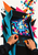 Tabletop arcade cabinet with a colorful maze screen, hands on joystick and button, and pixel-like shapes scattering upward.