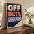 Three lines of raised fabric lettering read OFF DUTY, DREAMING on navy woven cloth, with an ivory quilted blanket corner at lower right.; frame shown for styling only