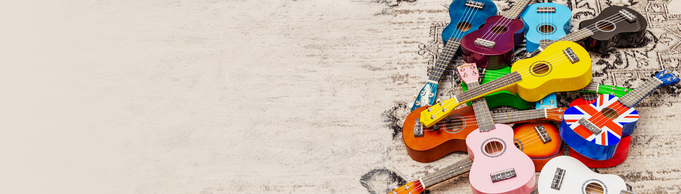 A vibrant collection of Tiger soprano ukuleles in assorted colors including pastel pink, blue, purple, yellow, orange, green, black, white, and a Union Jack design, arranged on a textured beige surface&mdash;ideal for beginners and music education school