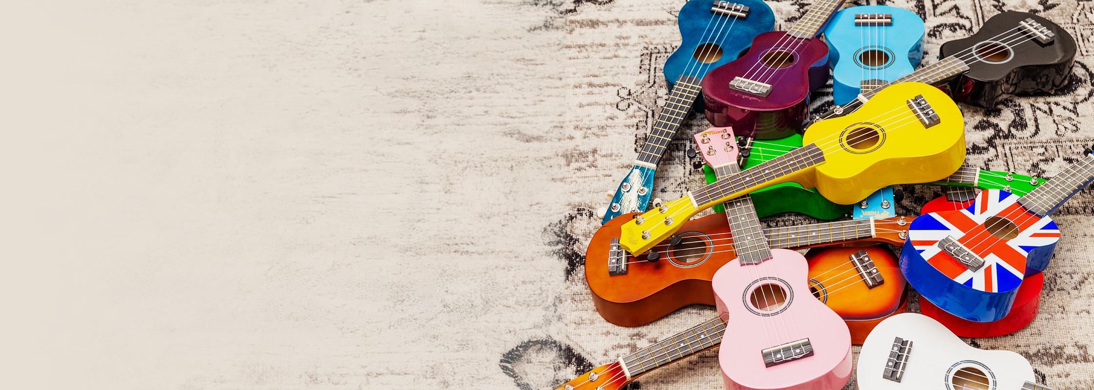 A vibrant collection of Tiger soprano ukuleles in assorted colors including pastel pink, blue, purple, yellow, orange, green, black, white, and a Union Jack design, arranged on a textured beige surface&mdash;ideal for beginners and music education school