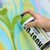 A hand holding a green spray paint can in front of colorful wall art.
