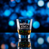 Wholesale engraved 1.75 oz. The Standard Shot Glass customized with Brentford Distillers logo on a bokeh background