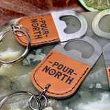 Wholesale engraved Oval Cognac Keychain Bottle Opener customized with Pour North Distillery logo on a black background