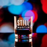 Wholesale engraved 8.5 oz. Stolzle New York Bar Rocks Glass customized with Still Austin Whiskey logo on a bokeh background