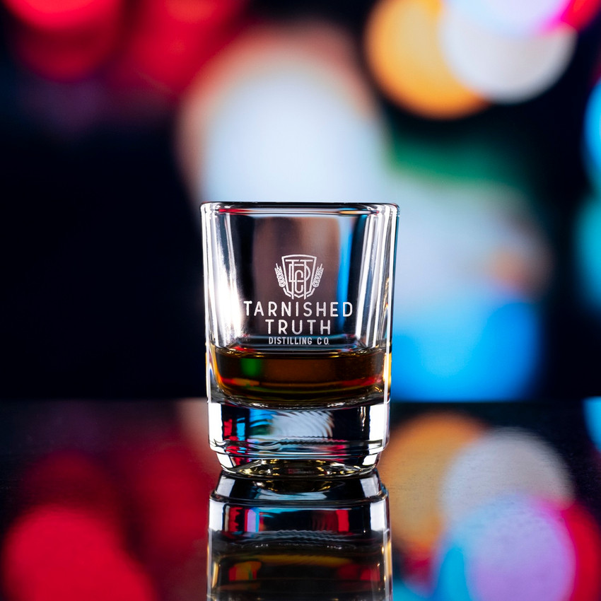 Wholesale engraved 2 oz. Small Batch Shot Glass customized Tarnished Truth Distillers logo on a bokeh background