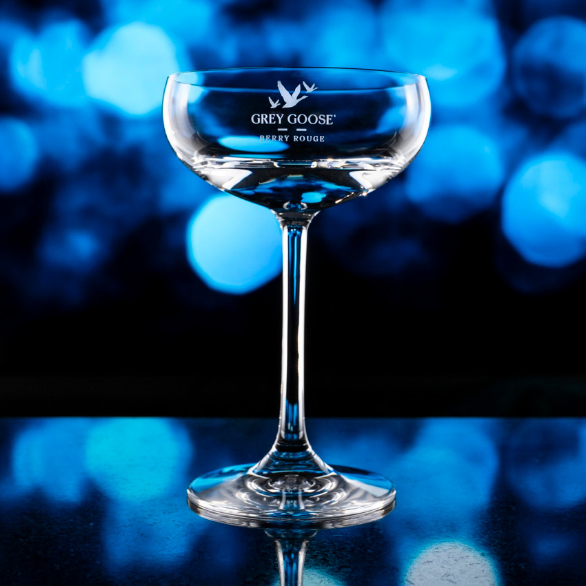 Wholesale engraved 7.75 oz. Stolzle Coupe Glass customized with Grey Goose logo on a bokeh background