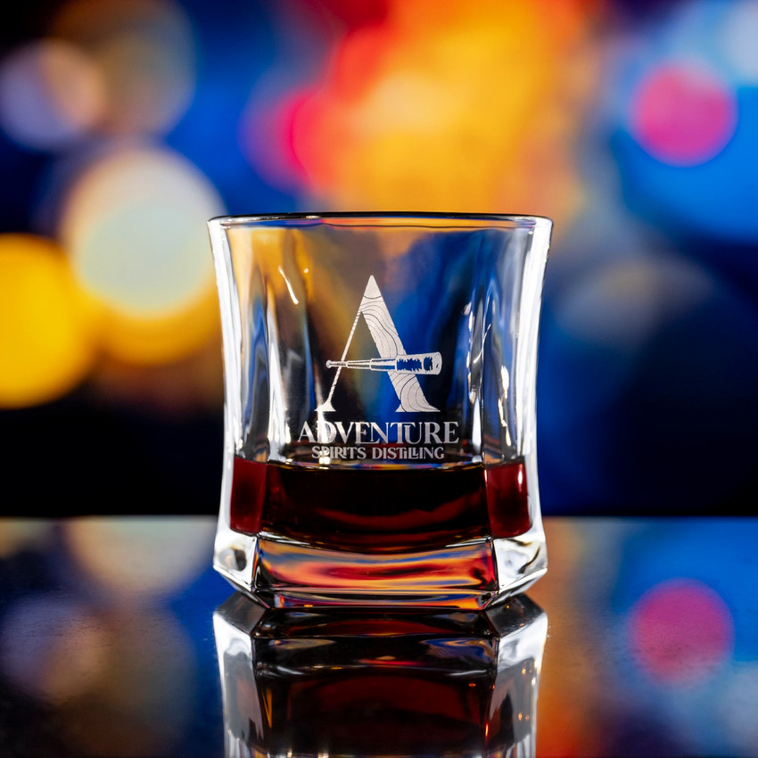 Wholesale engraved 10 oz. Le' Roxx Whiskey Glass with Adventure Spirits Distilling logo on a bokeh background