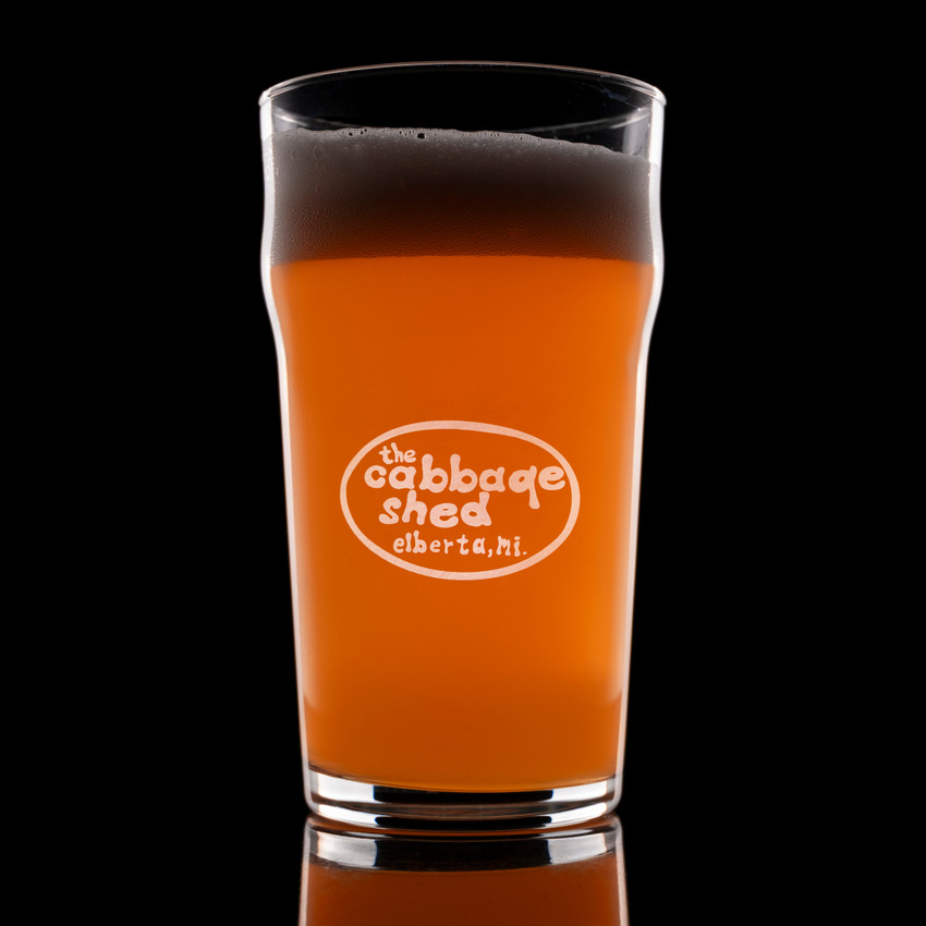 Wholesale engraved 20 oz. English Nonic Pub Glass customized with Cabbage Shed logo on a black background