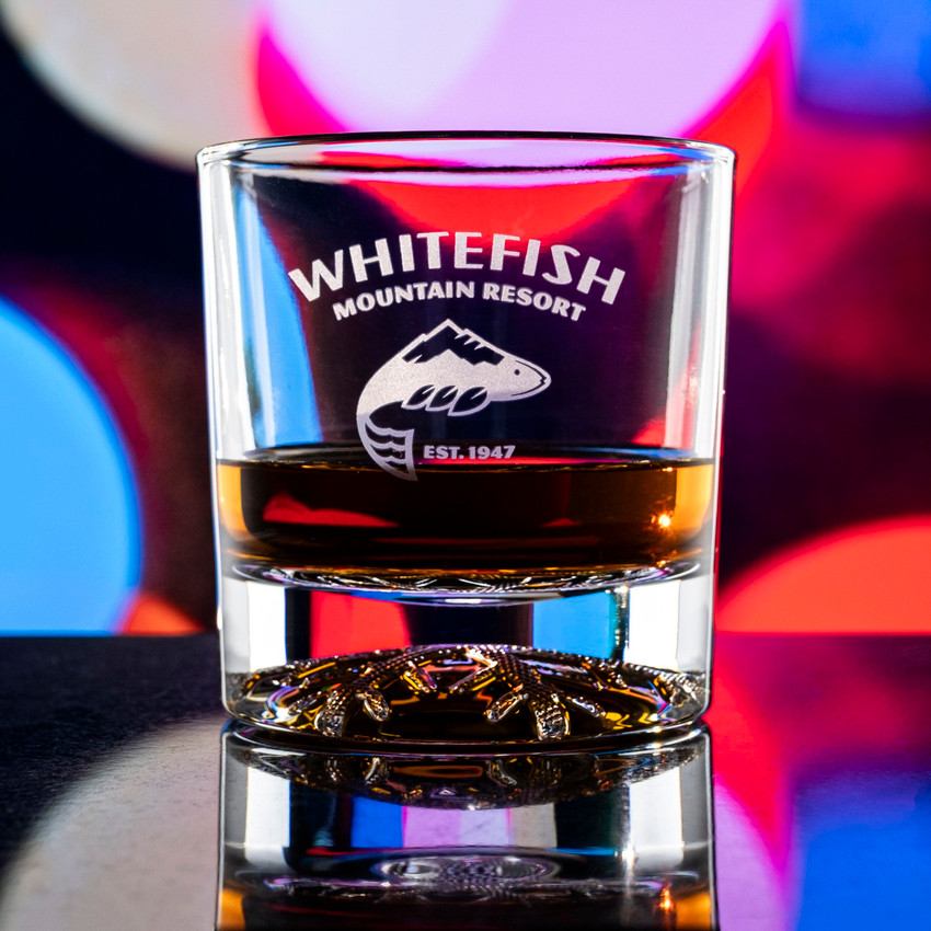 Wholesale engraved 10.5 oz. Snowflake Rocks Glass customized with Whitefish Mountain Resort logo on a bokeh background