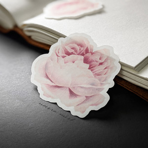 Pink rose sticker laying against an open journal. Pink rose sticker laying against an open journal.