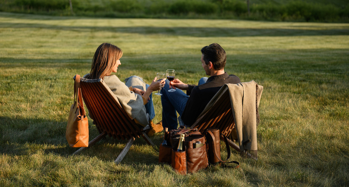 A couple enjoying wine in a field surrounded by Moore & Giles products