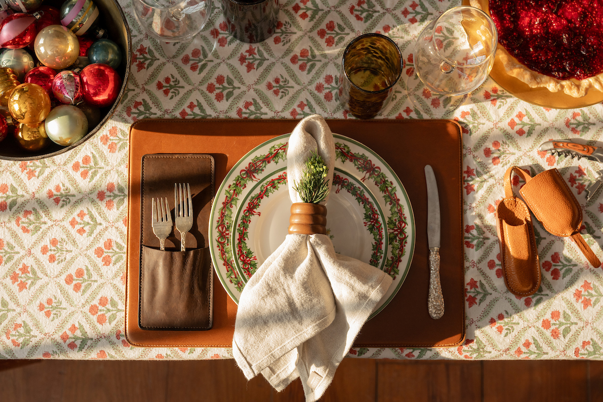 Holiday themed dining table with leather placemat, cutlery, and place setting.