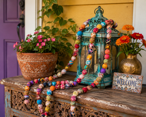 Colorful recycled sari bead garland draped across a boho porch display with vibrant fabric-wrapped beads, plants, lantern and eclectic decor.