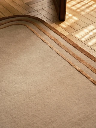 Arc rug in Amber, corner detail on a sunlit herringbone wood floor