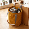 A yellow tote bag with grey straps, filled with towels, headphones, and a drink bottle, positioned near a table.