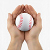 A white baseball with red stitching held between two hands. The hands are open, supporting the ball gently.
