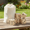 A wooden yard dice set with five large dice and a drawstring canvas bag, set on a wooden table outdoors.