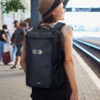 A black convertible travel backpack with a logo, worn by a woman at a train station.