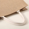A beige tote bag with white rope handles, featuring a textured fabric finish.