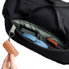 A close-up of a black duffel bag's interior, featuring a blue headset, a gadget, and a brown leather keychain.