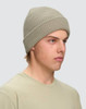A beige cable knit snug beanie displayed on a model, featuring a ribbed design and a logo.
