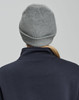 A grey cable knit beanie with a rolled cuff, seen from the back, worn by a person in a navy top.