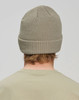 A roll-up cable knit snug beanie in a light khaki colour, viewed from the back. Features a ribbed band and a logo.