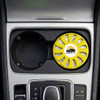 A round, yellow air freshener is placed in a car cup holder, featuring a logo and a vented design.