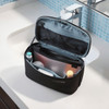 A black toiletry bag with a removable pouch, featuring various personal care items inside, displayed on a bathroom countertop.