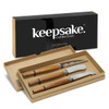 A set of three cheese knives with wooden handles in a gift box, featuring a black branding logo.