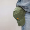 A vintage washed cap in green with a logo, resting against denim jeans.
