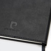 A black diary with a textured cover and a logo embossed on the front. It has a ribbon bookmark.