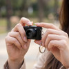 A compact black camera held in a person's hand, featuring a keychain attachment.