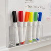 A display of seven Bonack whiteboard markers in various colours, including black, red, orange, yellow, green, and blue, stored in a clear holder.