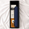 A navy umbrella is nestled in a box with treats like cinnamon balls and other snacks. The box has a sleek design and logo.