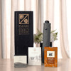 A grey umbrella stands beside packaged tea and coffee products, all displayed in a black box, with flowers in the background.