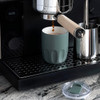 A drink bottle in a muted green colour with a ceramic liner, placed near an espresso machine on a black countertop.