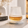 A drink bottle with a ribbed clear glass design sits on a marble coaster, featuring a golden liquid inside.