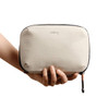 A hand holds a tan Bellroy Lite Tech Kit, featuring a soft-textured exterior and a zip closure.