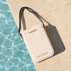 A beige cooler bag with a grey strap sits on a light stone surface next to blue water. It features a logo.