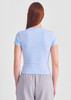 A women's baby tee in light blue, featuring a fitted design and short sleeves, worn with grey bottoms.