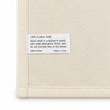 A cream cotton tea towel featuring a care label with washing instructions and a brand logo.