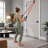 A person in a green fitness outfit using red resistance bands attached to a door, in a modern living room setting.