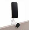 A silver phone holder with a black circular base, securely attached to a surface, holding a smartphone.