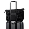 A black tote bag perched on top of a grey suitcase, featuring handles and a strap for carrying.