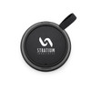 A round black speaker with a textured surface and a strap, featuring a logo on the front.